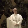A smiling man in a white cassock stands before The Resurrection sculpture.