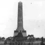 The Soviet War Memorial Schönholzer Heide with a tall stone obelisk and seated statue, surrounded by people on the steps.