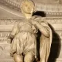 Marble statue of Saint Proculus standing in a short tunic and cloak among ornate stone carvings.