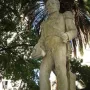 The Count of Porto Alegre monument, a light-colored military figure sculpture with epaulets and a sash, seen from below among trees and palm fronds.