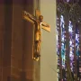Mindener Cross hanging on a wall beside a stained-glass window in a dimly lit interior.