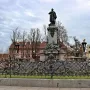 Adam Mickiewicz Monument showing a bronze cloaked figure on an ornate stone pedestal, with bare trees and wrought-iron fencing nearby.