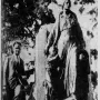 Man standing beside the Pioneer Mother Memorial sculpture showing a draped female figure with two smaller figures at her sides.