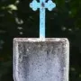 Weathered stone Padrão monument with a shield carving and blue cross, standing in grass and foliage.