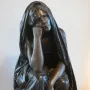 La Douleur, a dark metal sculpture of a draped figure with one hand to the cheek, standing on a plinth.