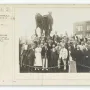 A large group of men and one woman pose in tiers in front of the George Washington monument.