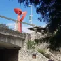La Antorcha de la Amistad rising above a stone wall beside the riverwalk under a blue sky.