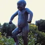 The Sinataggen bronze sculpture of a toddler stamping its foot on a pedestal, surrounded by trees.