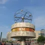 The World Time Clock in Berlin, with city names and illuminated time panels beneath a spherical metal top in a public plaza.