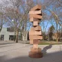 Endlose Treppe by Max Bill, a tall reddish-brown stone sculpture on a paved plaza with trees and a modern building behind it.