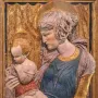 Painted terracotta Madonna and Child relief in a dark frame behind reflective glass.