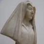 Bust of Camilla Barbadori in light-colored marble, showing a woman with a draped head covering and a dark pedestal.