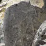 Karasu relief carved on a weathered dark stone slab among larger rocks.