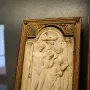 Queriniano Diptych ivory panel with a carved standing man and woman, a cherub, and a small animal beneath a shell-topped arch.