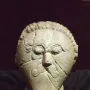 Mšecké Žehrovice Head showing a carved stone face with oval eyes, a curled mustache, and a braided headdress.