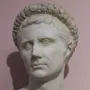 Bust of Augustus wearing a gemmed crown, shown in profile against a stone wall.
