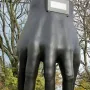 Hand with Clock sculpture on a tall pedestal beside a digital time display, with trees, bicycles, and a nearby building in the background.
