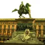 Victor Emmanuel II Monument with an equestrian statue above a carved pedestal, a crowned lion below, and a building in the background.