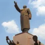 Bronze monument of Mao Zedong with his right arm raised, surrounded by smaller figures at the base.