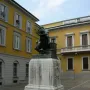 Bronze monument to Mose Bianchi showing a seated bearded man holding a painter\'s palette on a stone pedestal.