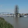 Quantum Cloud sculpture on a riverside platform beside a blue pedestrian bridge.