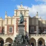 Adam Mickiewicz Monument on a tall pedestal in Krakow’s market square, with the Cloth Hall and people in the background.