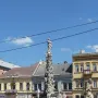 Marian Column with a haloed statue of the Virgin Mary, surrounded by figures and a metal fence.