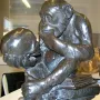 Bronze sculpture of a chimpanzee holding a human skull while seated on books, including one labeled Darwin.