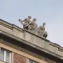 Stone sculpture of three figures representing Music, seen from below against a clear sky.