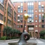 Erich-Schulze-Brunnen, a dark metal fountain with a curved trumpet-like form topped by a gold sphere in a paved courtyard.