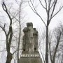 War Never Again stone monument showing a man embracing a woman and child on a tiered base inscribed “NIGDY WOJNY.”