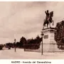 Marqués del Duero monument beside a wide tree-lined avenue in Madrid, with a fence and buildings in the background.
