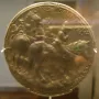 Medal of John VIII Palaiologos showing a round gold-colored relief with figures on horseback and inscriptions around the edge.