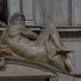 Michelangelo’s Day, a reclining marble male figure with drapery over the lower body.