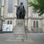 The New Bach Monument statue of Johann Sebastian Bach standing beside a stone building with one hand raised.