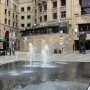 Nelson Mandela statue with raised arms in a busy public square, standing behind a fountain.