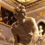 Bernini\'s David marble statue shown in a gallery interior, holding a sling and looking to the side.