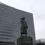 Marco Polo statue on a stone pedestal in front of a modern building.