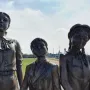 Kindertransport bronze sculpture of three children standing outdoors near a road and grassy area.