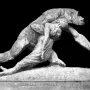 Gorilla Carries a Woman sculpture showing a gorilla standing upright with a woman slung over its shoulder, holding a rock on a rocky base.