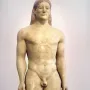 The Kroisos Kouros, a nude male marble statue standing with arms at its sides and braided hair.