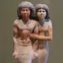 Painted ancient Egyptian statue of Raherka and Meresankh standing together on a rectangular base.