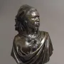 The Nubian Man bronze sculpture shown in three-quarter view on a dark pedestal, with a textured beard, draped garment, and tied head covering.