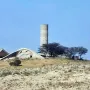 The Monument to the Negev Brigade, with a tall cylindrical concrete tower and sculptural low concrete forms on a barren hill.