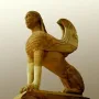 Sphinx of Naxos stone sculpture with a woman\'s head, lion\'s body, and carved wings on an ornate volute base.