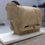 Stone sculpture of the Bull of Osuna in a resting pose on a white display stand.