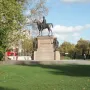 Duke of Wellington statue on a stone pedestal, with smaller figures at the base in a park setting.