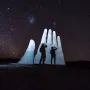 Mano del Desierto sculpture lit against a star-filled night sky, with two people standing in front of it.