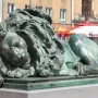 Sleeping Lion bronze sculpture with a green patina, shown lying with its head resting on its front paws.