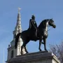 Equestrian statue of George IV on a stone pedestal, with a church steeple and clock tower behind it.
